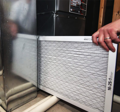 A hand sliding a new pleated air filter into a furnace
